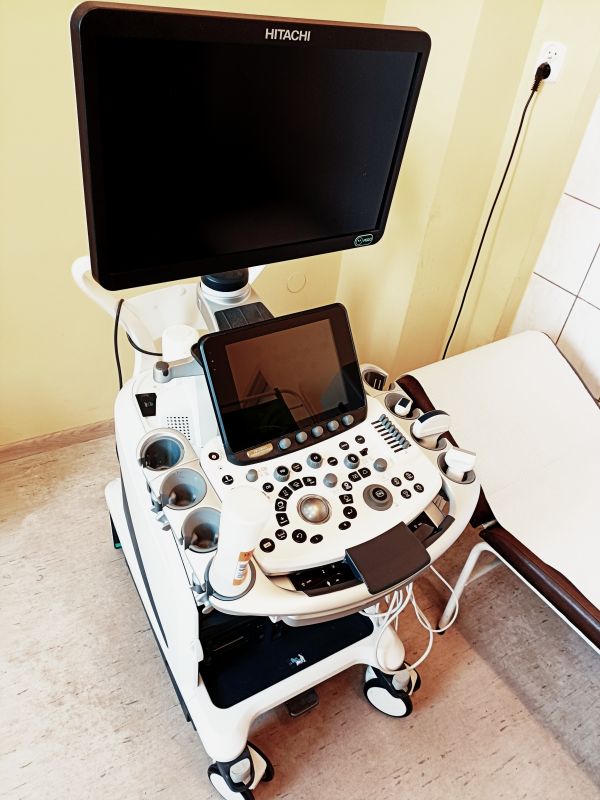 Aparat USG z przodu, ustawiony koło leżanki.